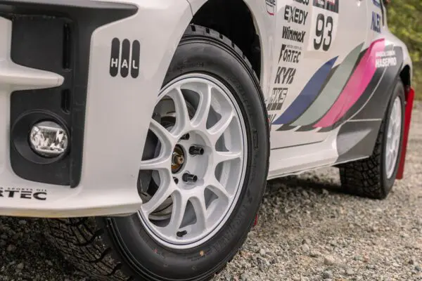 A white rally car is parked on a gravel road.
